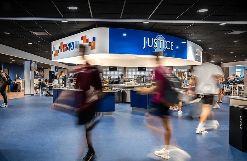 Two students sit at a table with a red and white star, and SAU written on a blue wall in the background.