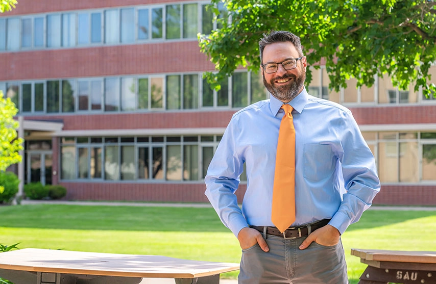 Jason Richter stands in front of a university building and under a tree.
