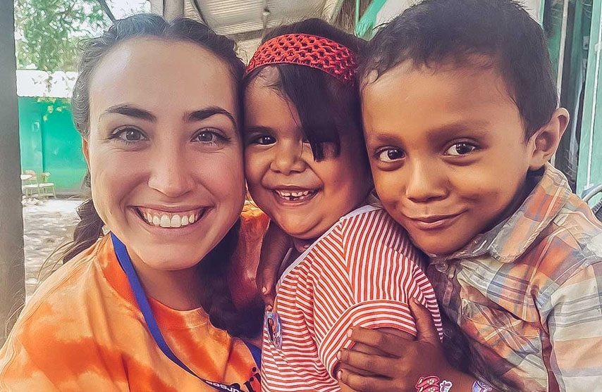 A woman in an orange shirt takes a selfie with two children.